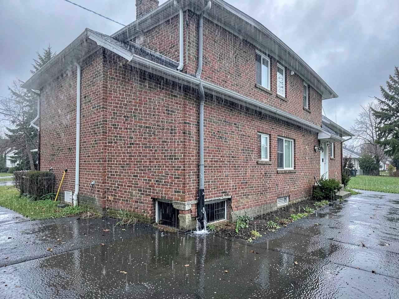Rainwater pooling against the foundation of a brick house during a storm